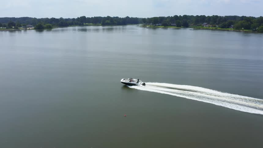 A boat sails across the water and the coast is lined with forests of trees