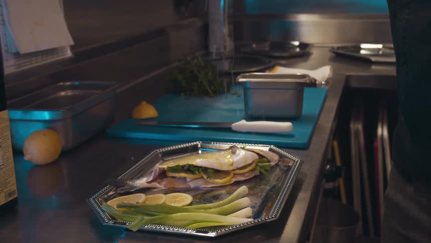 A person in commercial kitchen sprinkles something on a platter of food