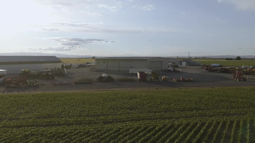 Ascending over newly planted clopland to reveal a large farm yard with machines and equipment parked near various buildings