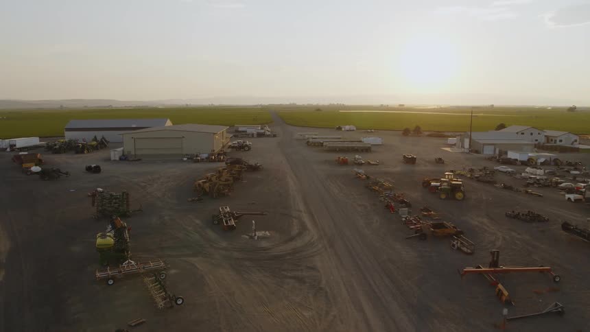 Traverse over a large farm yard compound filled with tractors, equipment and various buildings and sheds