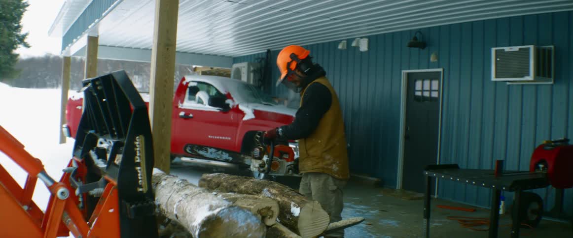 A man uses a chainsaw to cut wood on a farm