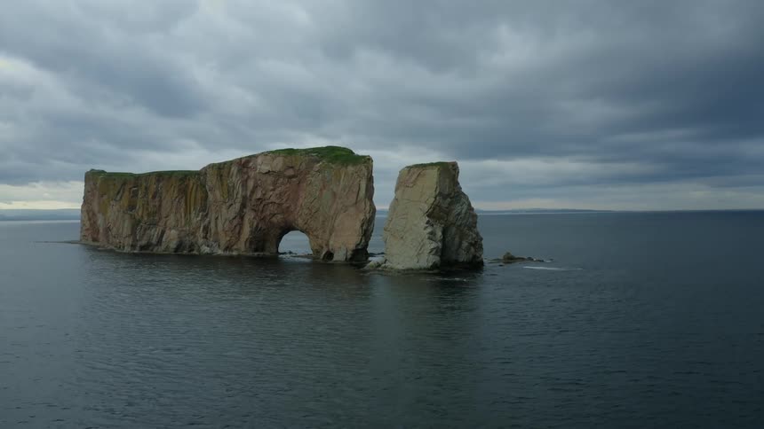 Ocean water passes through natural tunnels in islets standing in ocean under an overcast sky