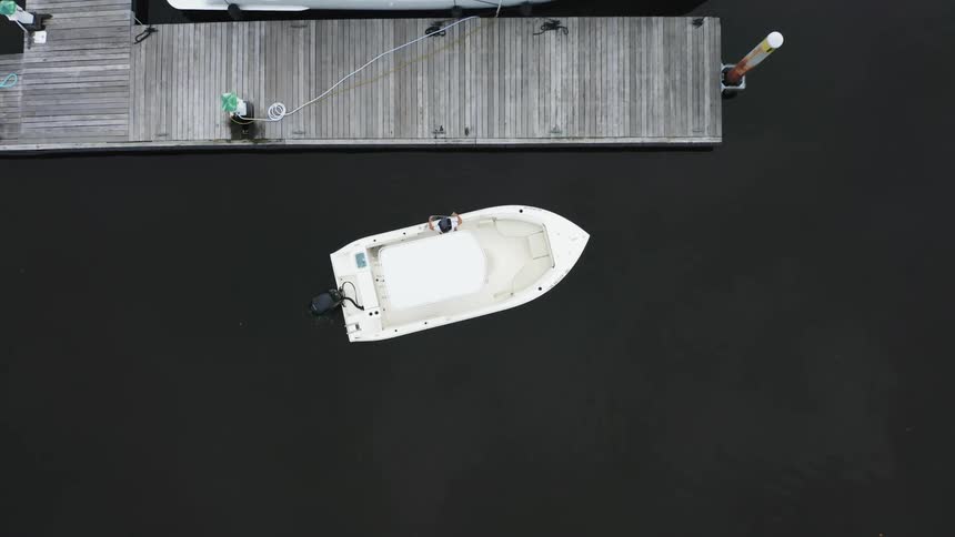 Person leans out of motorboat to toss rope over mooring post at pier