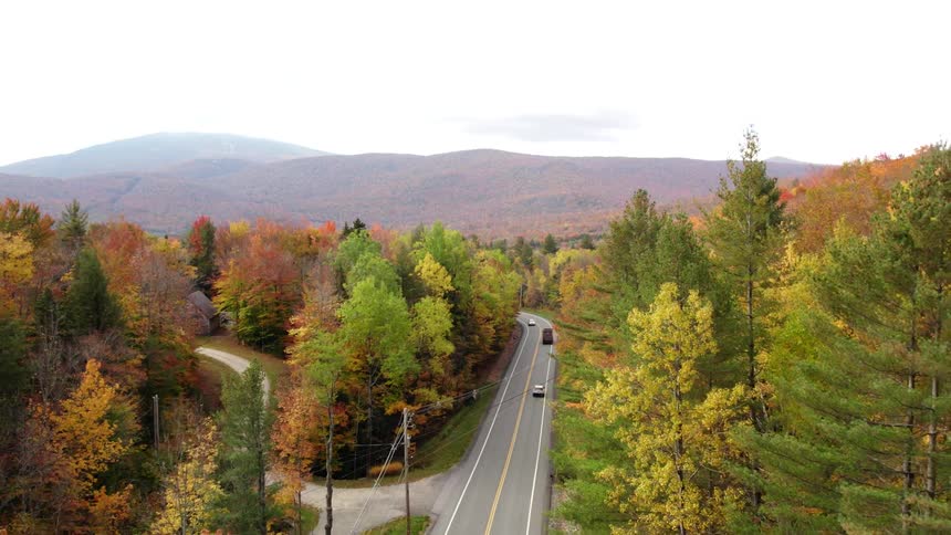 Traffic travels on a road running through a forest of trees in bright fall colors with mountains in the distance