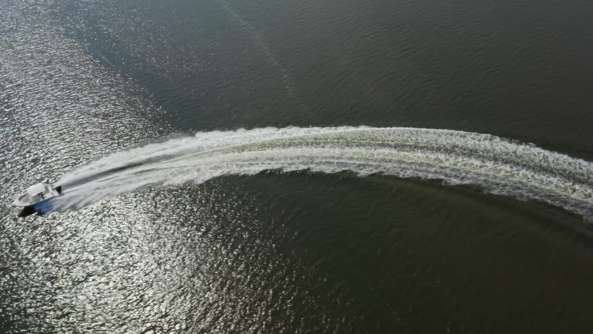 Aerial view of a small boat traveling across the water and the sun is reflecting light on the ripples in the water