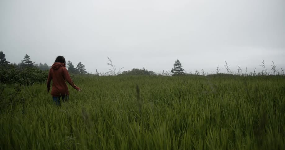 Woman with red hoodie and jeans walks in the tall grass