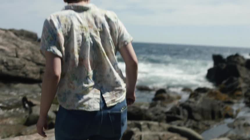 A man walks across a rocky beach towards the ocean water