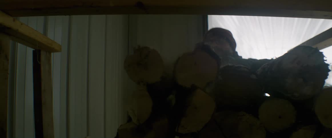 Man wearing knit hat stacks firewood logs into wooden frame