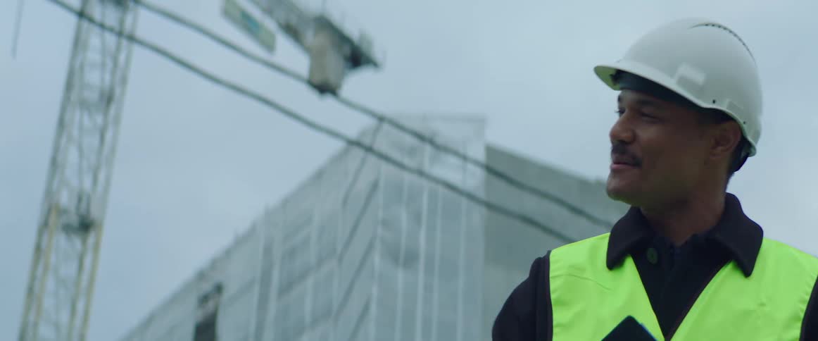Male construction worker wearing safety helmet and vest holding a clipboard and shaking the hand of a woman