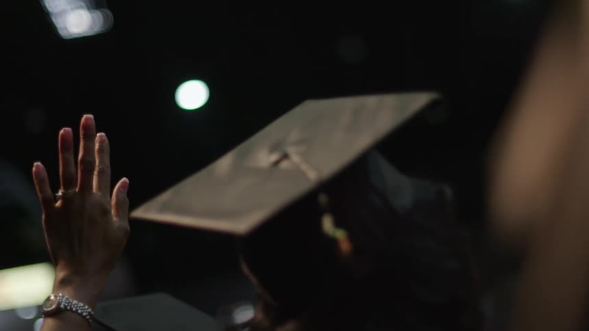 Graduating student waves while wearing a graduation hat at a graduation ceremony