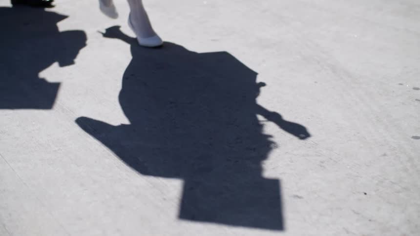 The sun casts the shadow of man and woman wearing graduate robes and a graduation cap onto the concrete