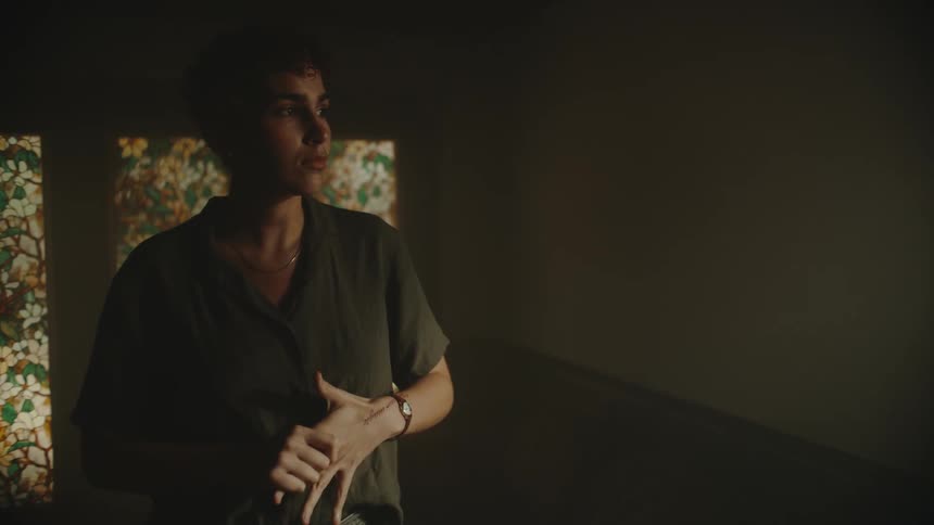 A teenage boy at homes wrings his hands in worry and looks out the window