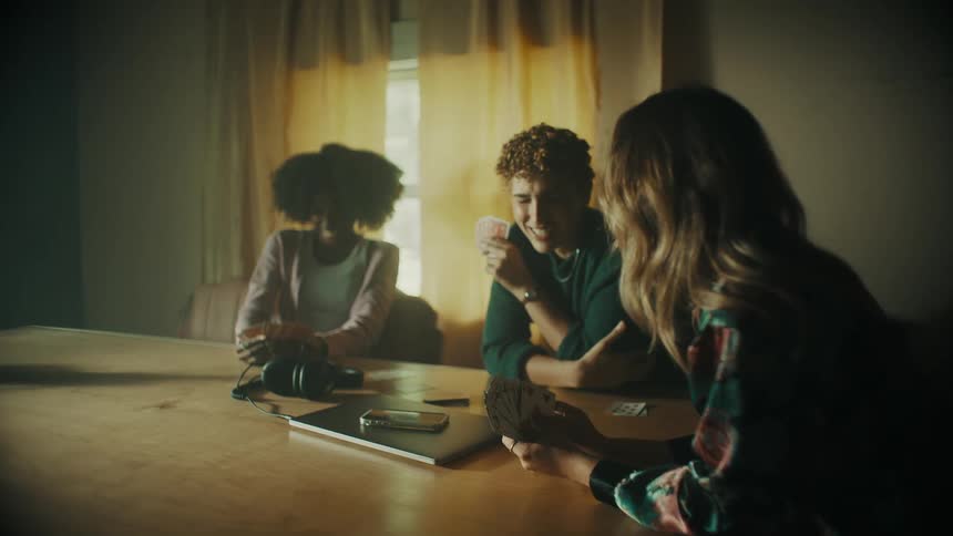 Three women sit a table playing a card game and laughing