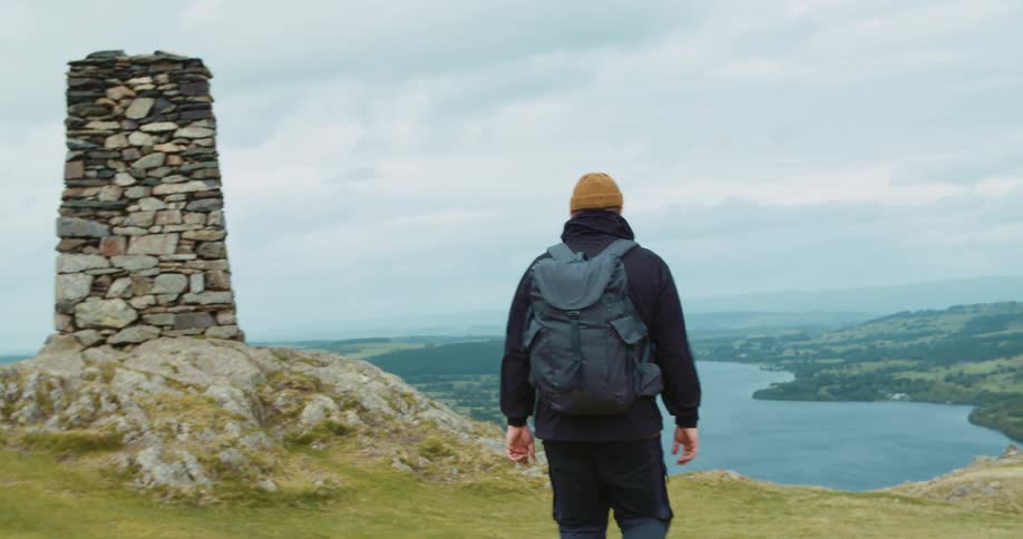 A man on a hill hikes towards a lake