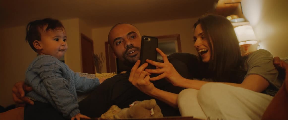 Mother father and baby sitting at the couch in the living room video calling someone else and smiling and laughing