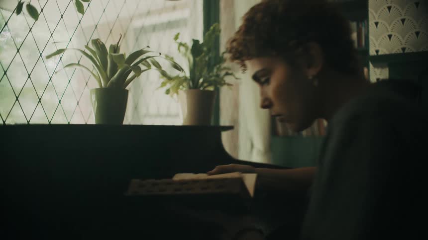 A woman picks a book out of a bookcase then carries it over to the writing desk to sit and read