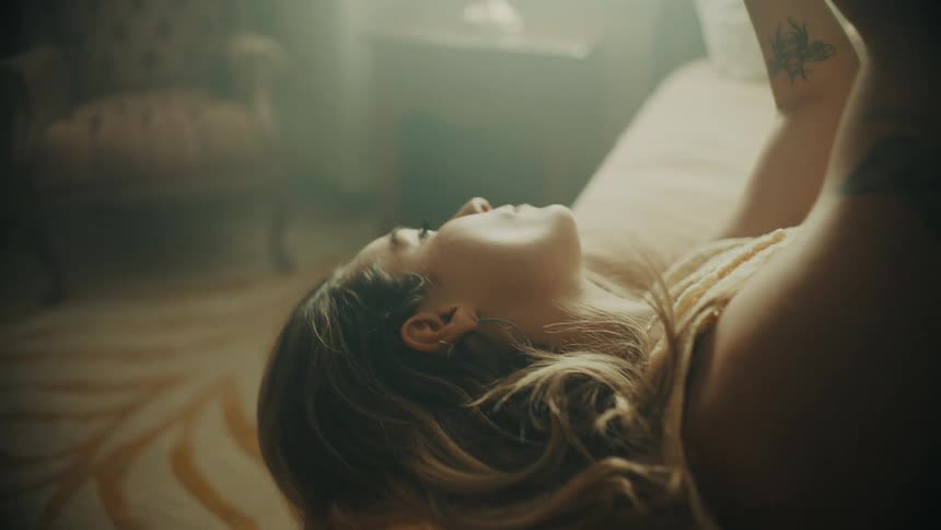 A woman lies in bed with her arms in the air