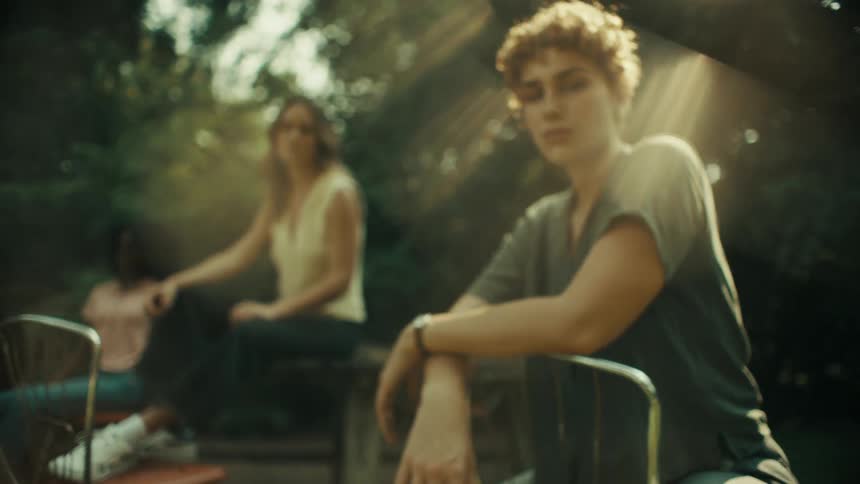 Three teenagers sit outside in a front yard as a car drives past