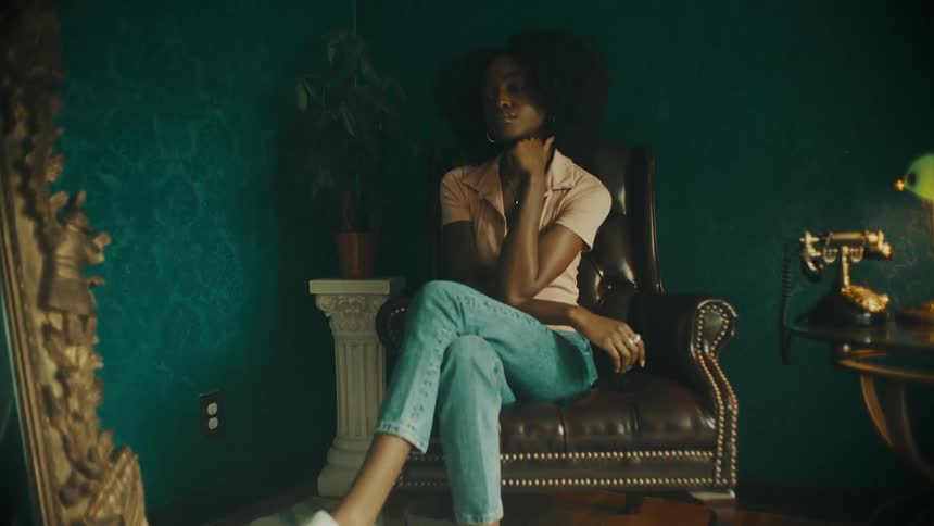 A teenage girl sits in a chair in a house and pushes her hair back