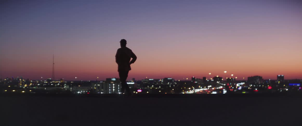 Man looking apprehensive walking in the top of a building during sunset with the view of a big city ahead