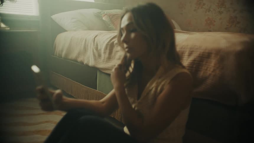 Young white woman sitting in the ground next to her bed on her bedroom taking selfies with her smartphone