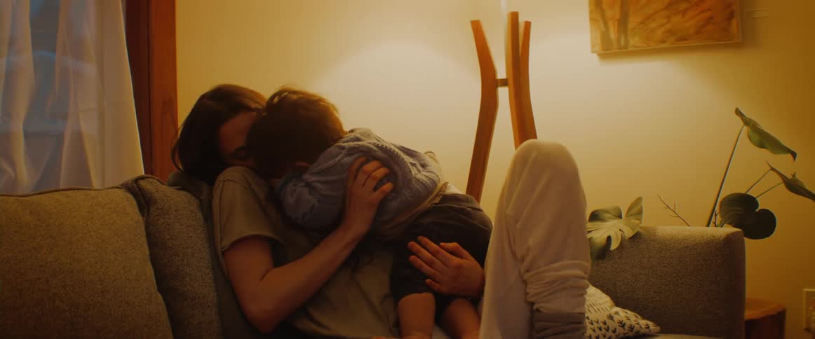 A woman sits on a couch cuddling with a small infant