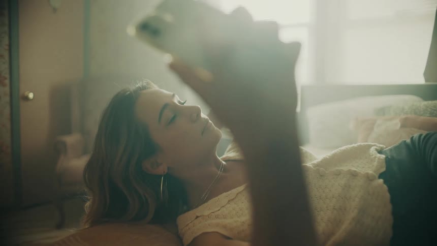 A woman takes photos of herself while lying in bed and posing