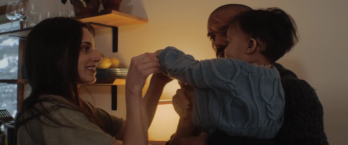 Mom hands baby some food while dad is holding him then rolls up his sweater sleeve