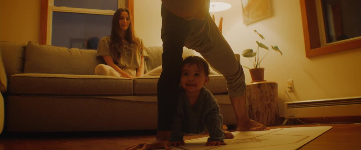 A man does yoga as his son crawls underneath him