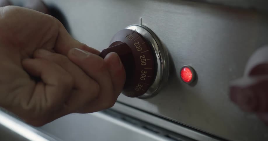 A hand turns the dial on an oven setting the temperature and a red light goes on
