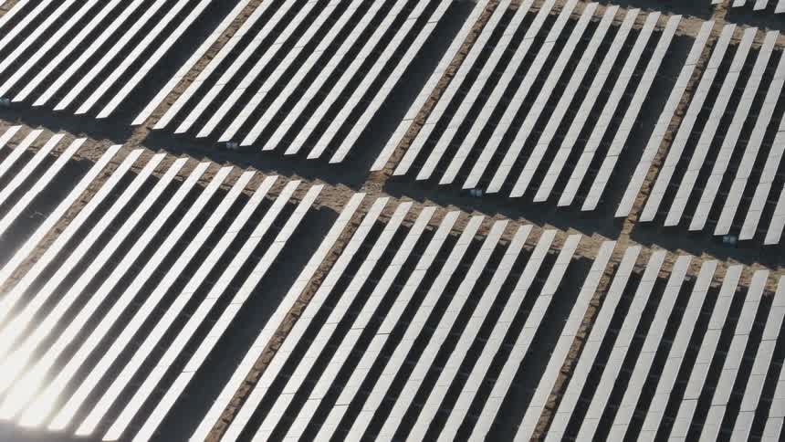 The sun is shining brightly on solar panels on a solar farm
