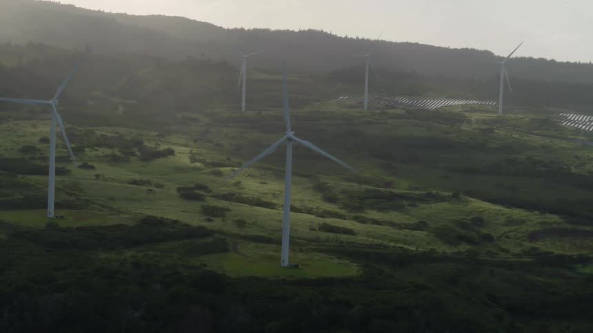 The sun is shining brightly as wind turbines are turning on a hillside