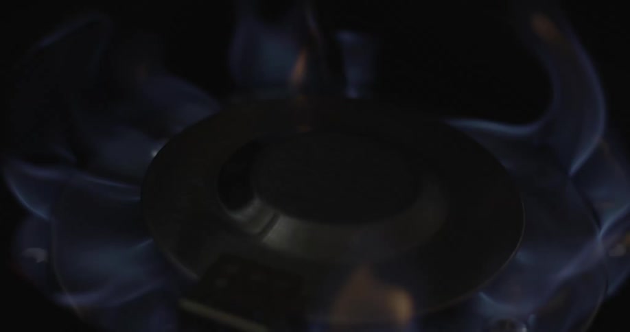 A flame ignites a burner on a gas stove and it is encircled with blue flames