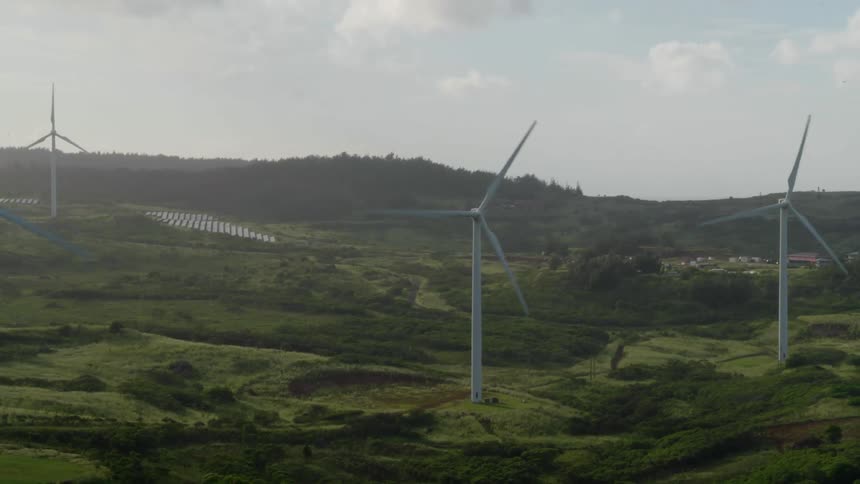 Wind turbines are turning on a hillside under a cloudy sky