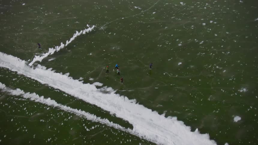 Birds eye view of people ice skating on a frozen lake below