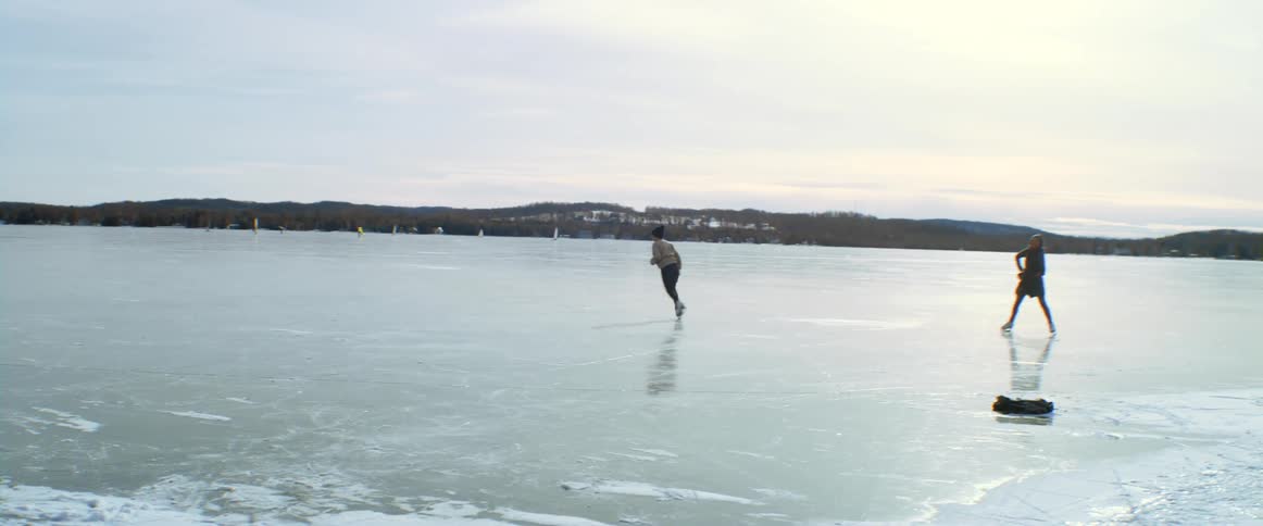 A woman ice skating on a lake spins around as her friend watches