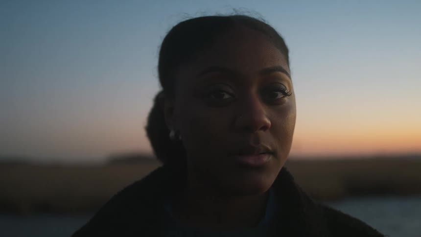 Woman with her hair in a bun faces the camera with eye contact outdoors