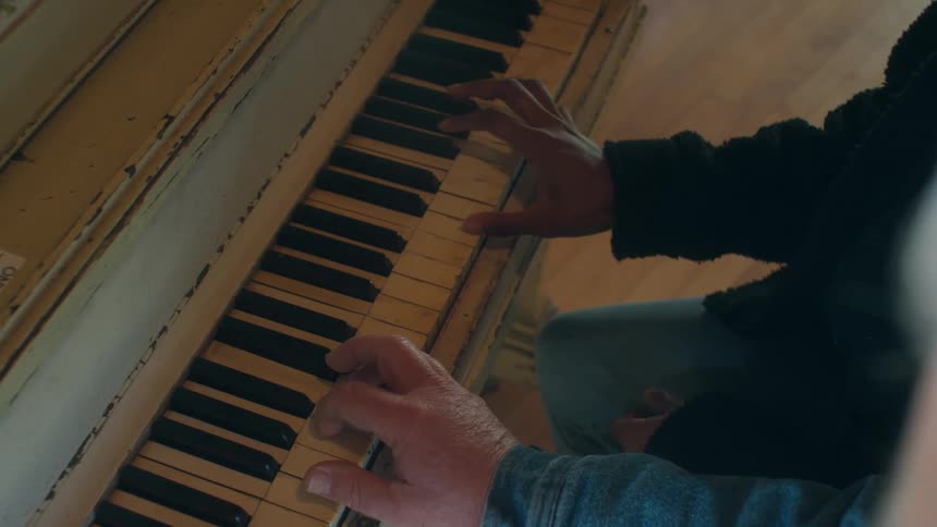 Elderly man with blue shirt and woman wearing black jacket play piano together