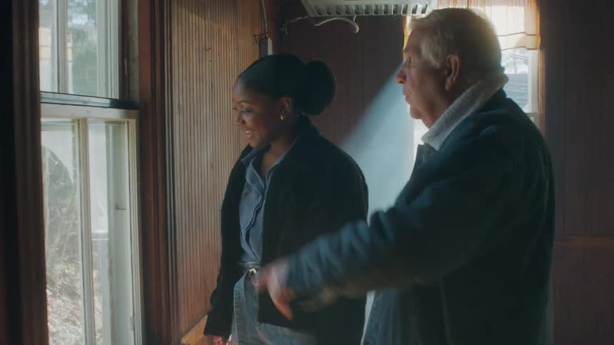 A man shows a woman the backyard view of a home from inside