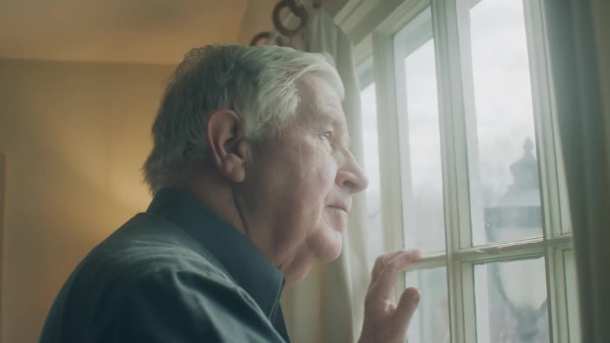 A man opens the curtains to a window and looks outside