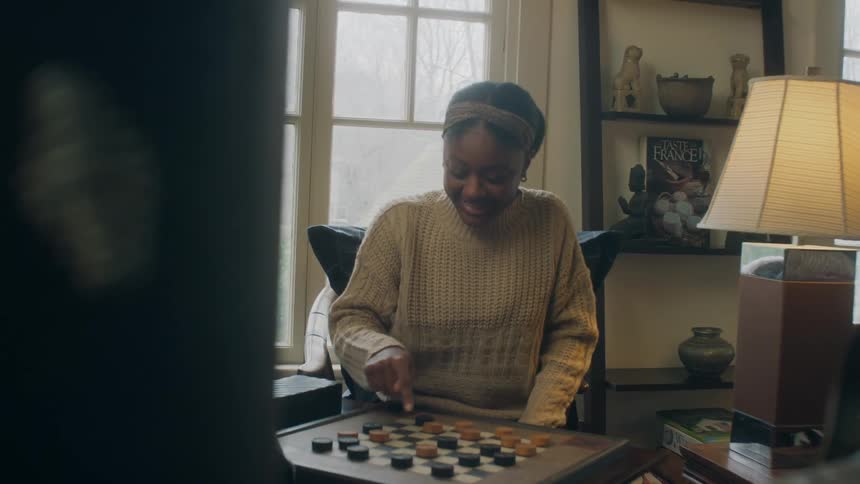 A young woman sits in a house with an elderly man and they play a game together