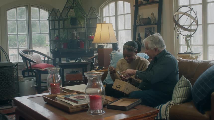 A young woman and senior citizen are sitting in a living room having conversation over photos in a box during the day