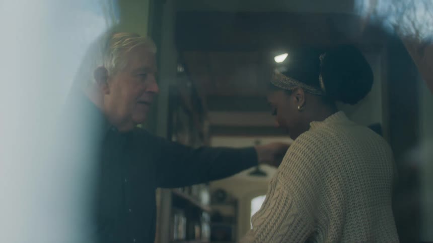 An elderly man dances with a young woman in a house