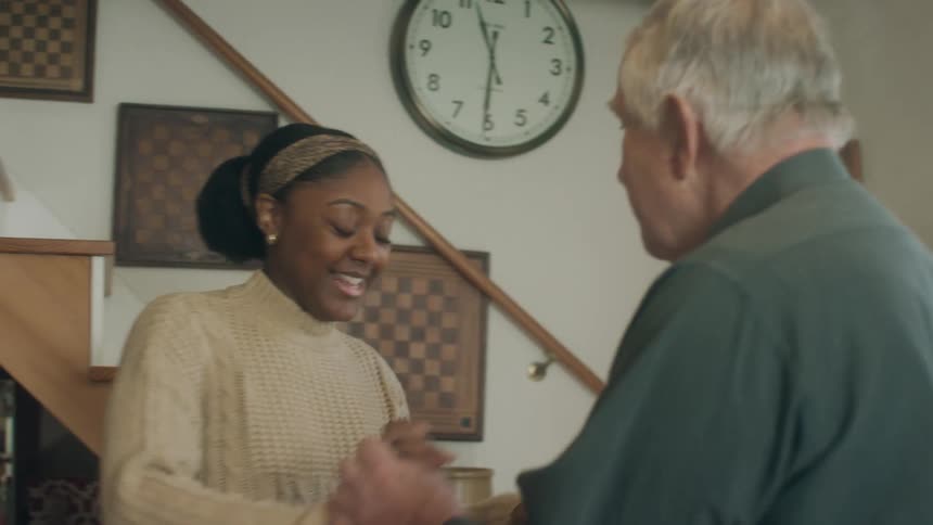 Man and woman smile and talk while dancing on wooden floor near stairs