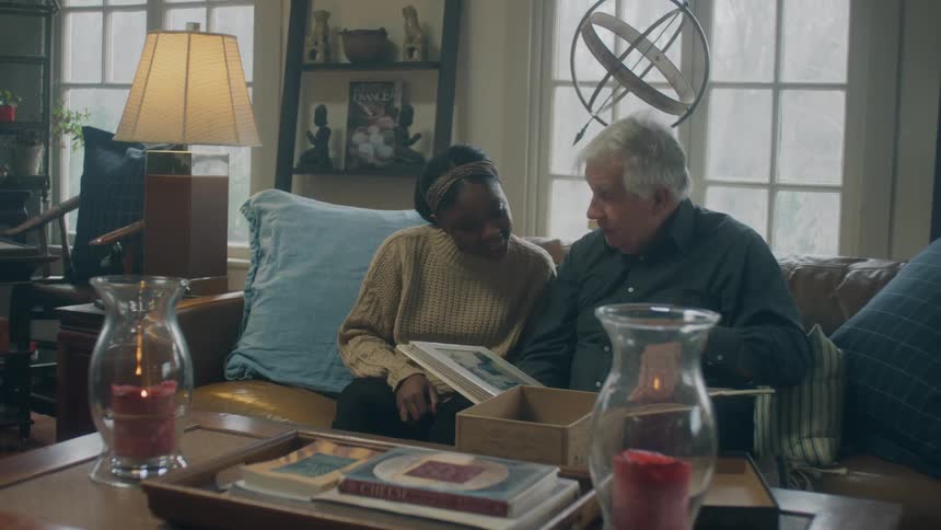 Elderly man and woman sit on sofa going through a photo album