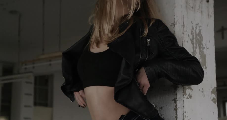 A woman in a black jacket leans against a chipped pillar as she dances