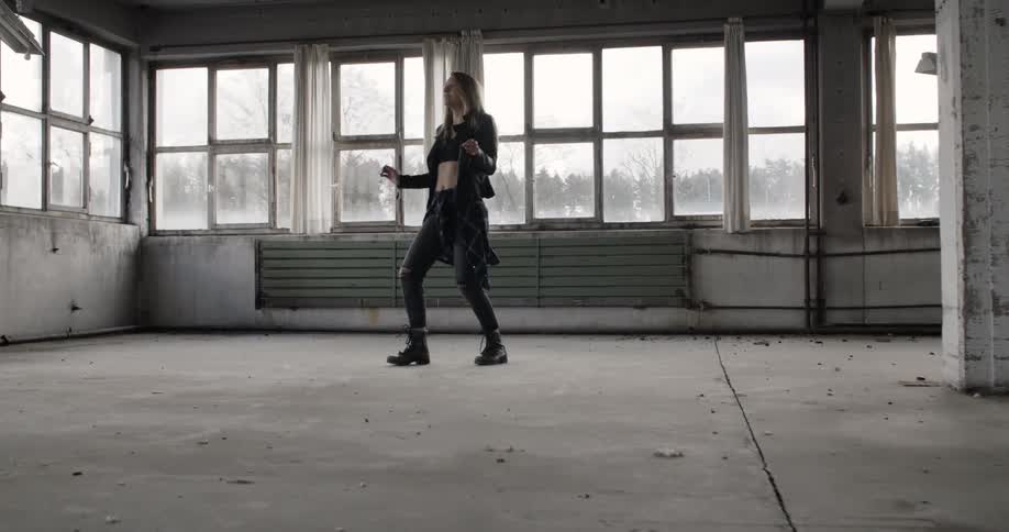 A woman dances by herself in a warehouse