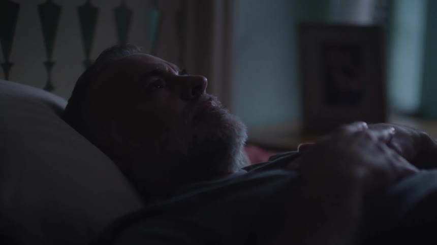 White man lying down in his bed with his hands on his chest looking to the ceiling