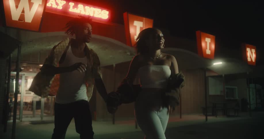 Couple holds hands as they run across parking lot outside a bowling alley at night