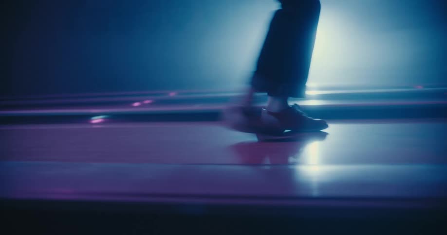 Male and female dancers move across glossy walkway under backlit by a spotlight